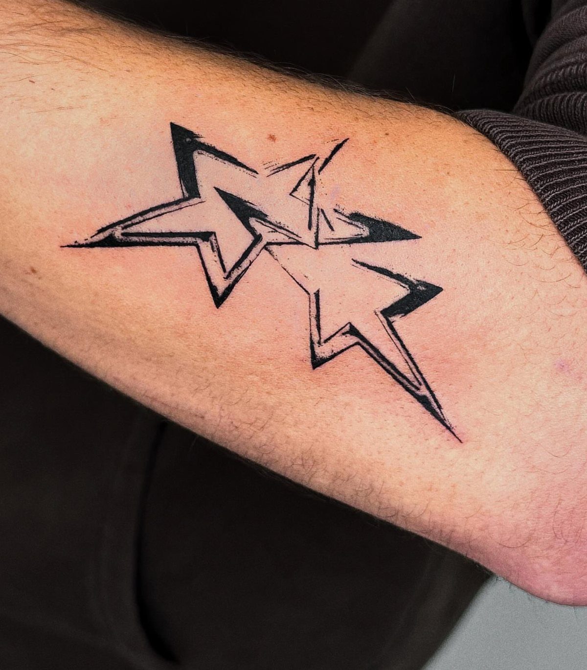Two geometric star tattoos with overlapping black lines on a person's forearm.