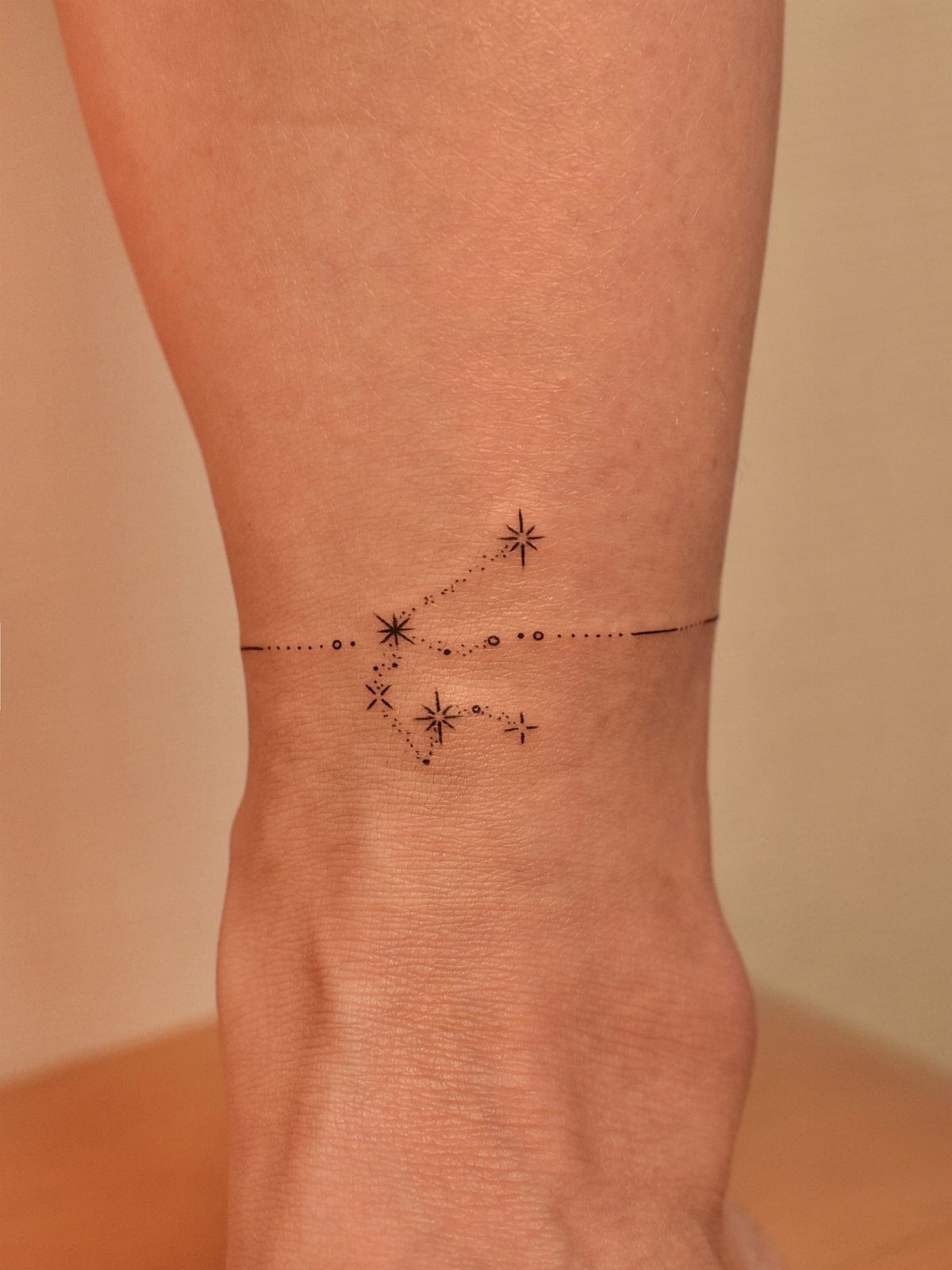 Small black ink star cluster tattoo on a person's ankle in a constellation pattern.