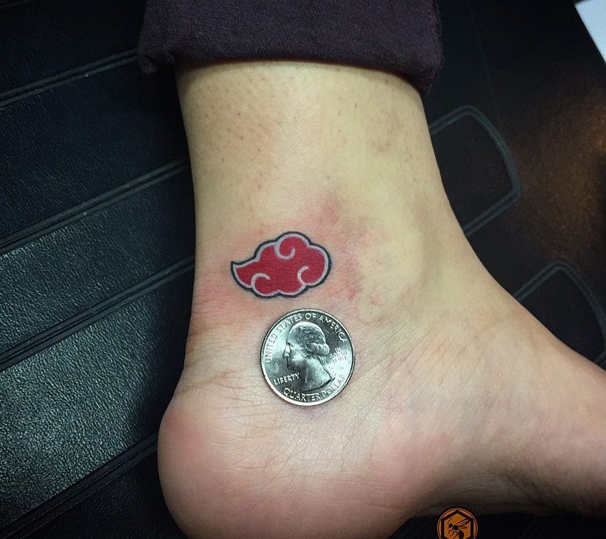 Red cloud tattoo with black outline on an ankle next to a quarter coin