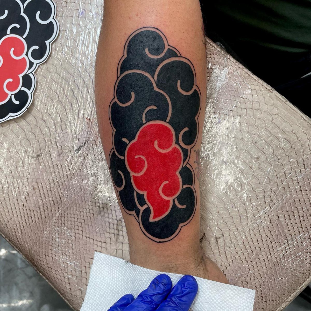 Stylized black and red cloud tattoo with swirling patterns on a forearm.