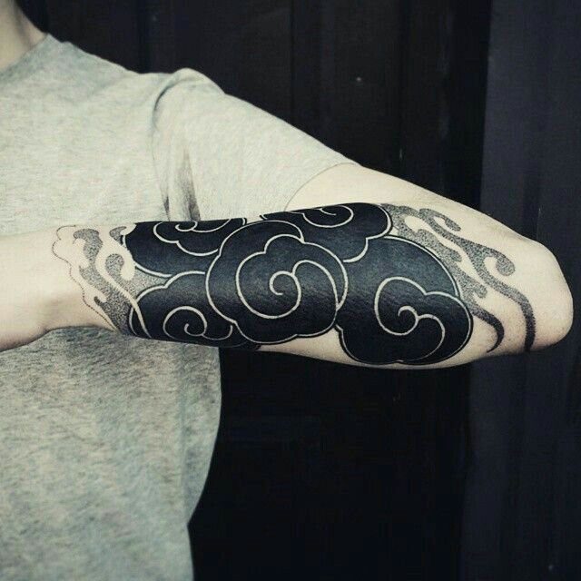 Black cloud tattoo with white outlines and swirls on a person's forearm