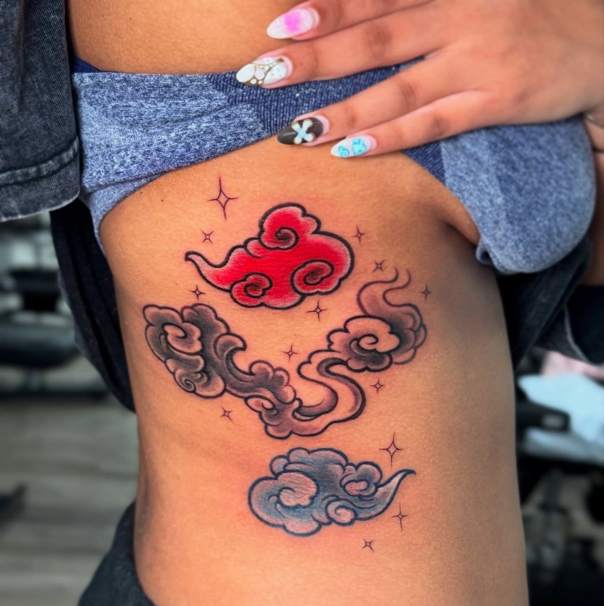 Stylized cloud tattoos in red, grey, and blue on a person's thigh.