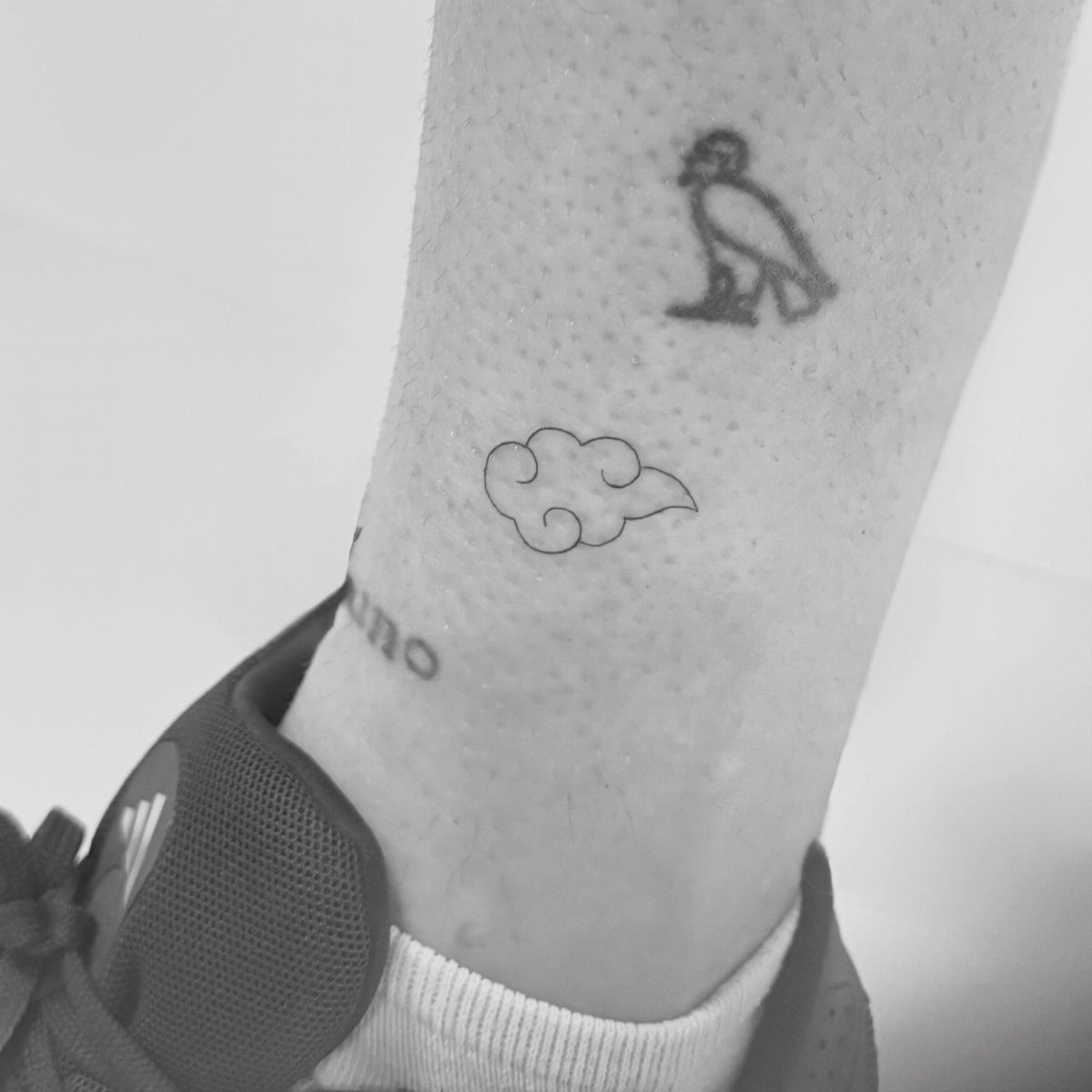 Small minimalist cloud tattoo outline on a person's ankle in black and white