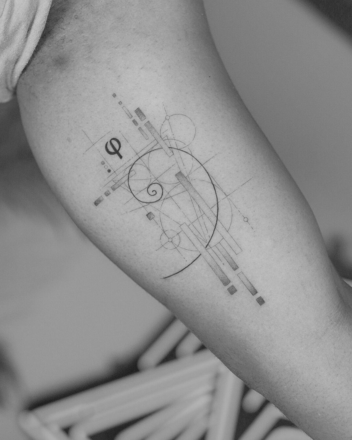 Fibonacci spiral tattoo with geometric lines and phi symbol on a person's arm.