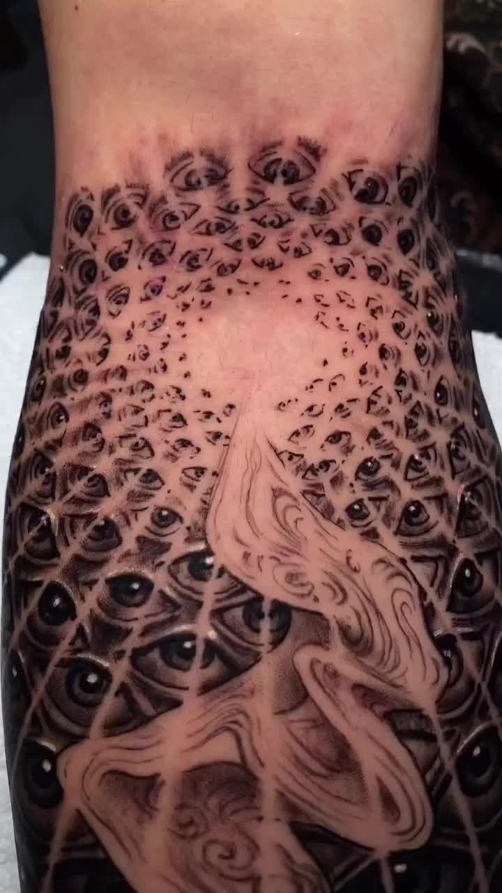 Tattoo of many small eyes in a geometric grid with flowing abstract shapes.