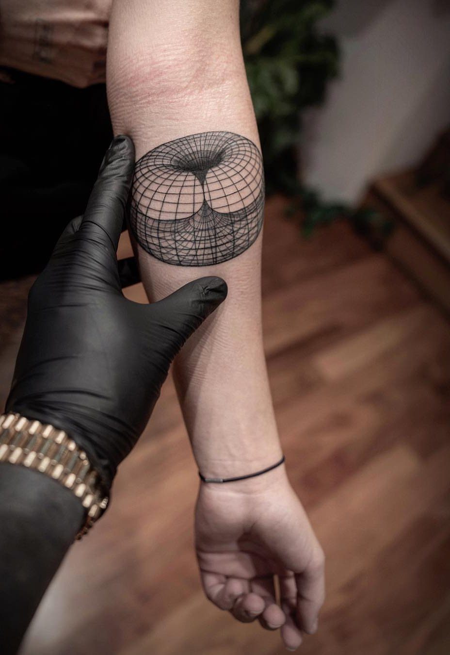 Torus grid tattoo on a forearm being held by a gloved hand.