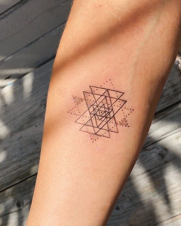 Geometric tattoo of interlocking triangles and dots on a person's forearm.