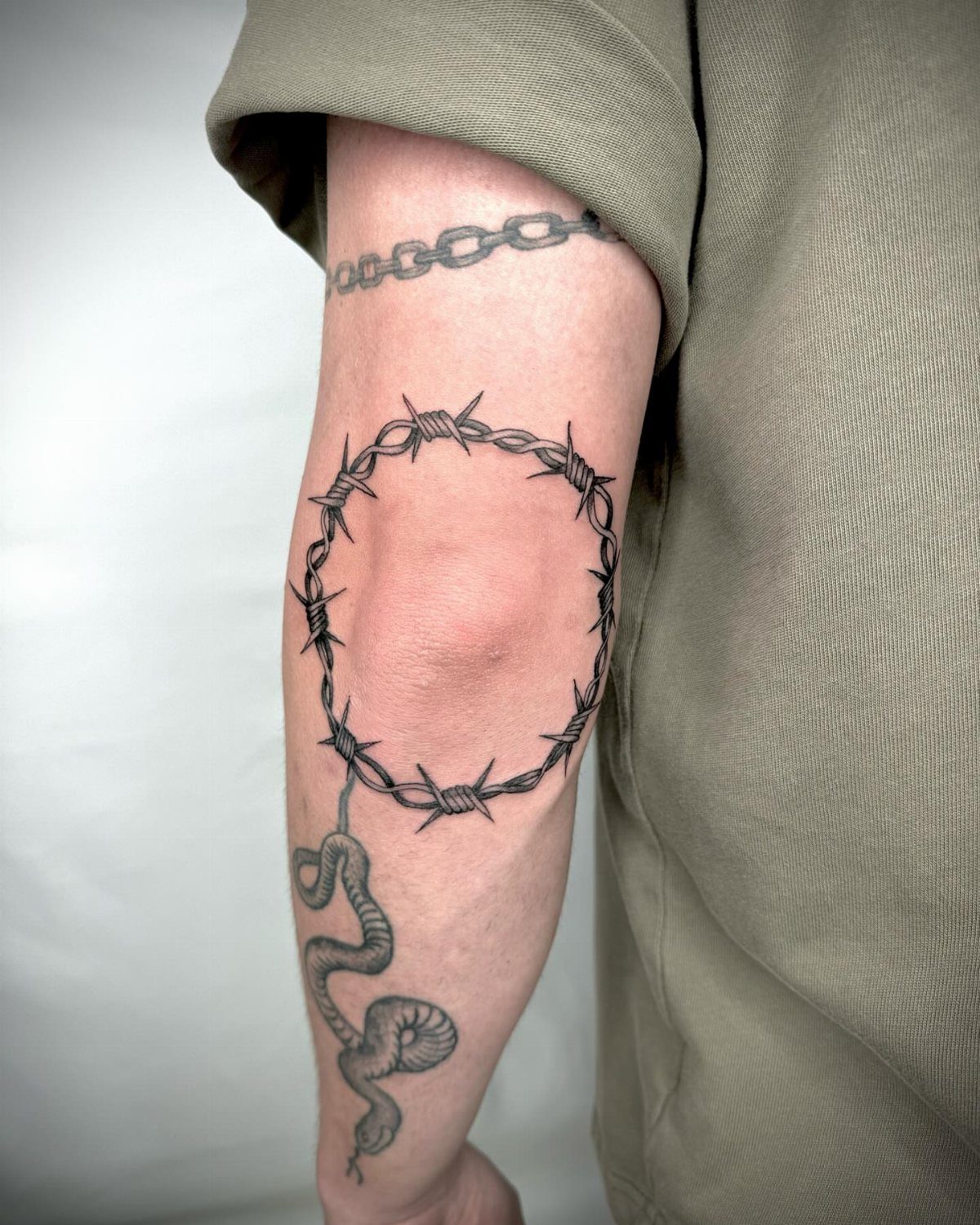 Barbed wire tattoo wrapped around a person's upper arm with a snake below.