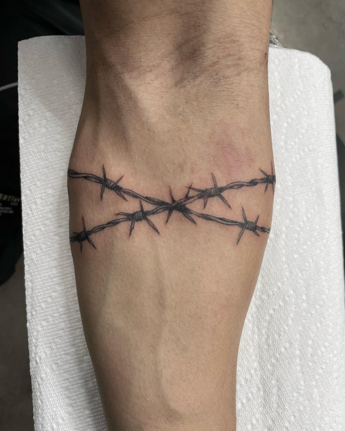 Barbed wire tattoo wrapped around a person's forearm on a white background