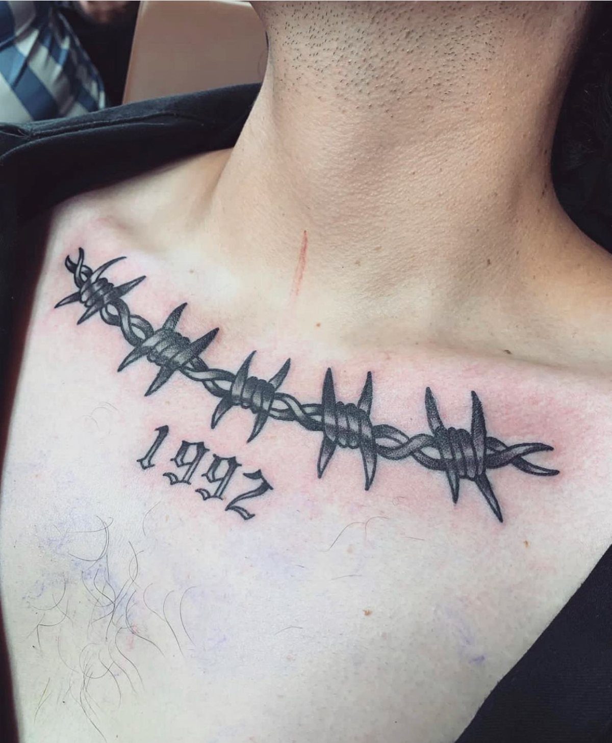Barbed wire tattoo and the year 1992 on a person's upper chest.