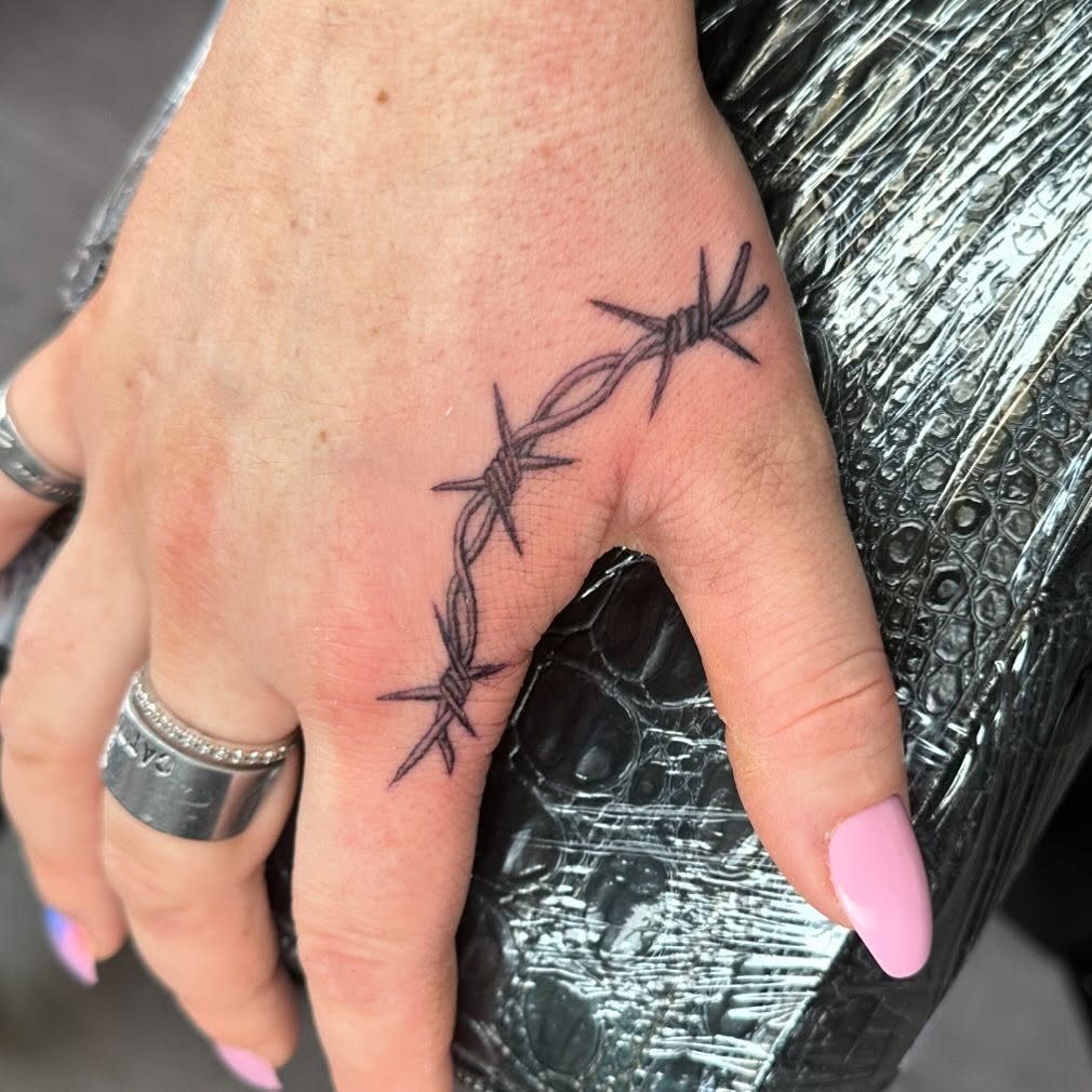 Barbed wire tattoo with fine lines curving across the back of a hand.