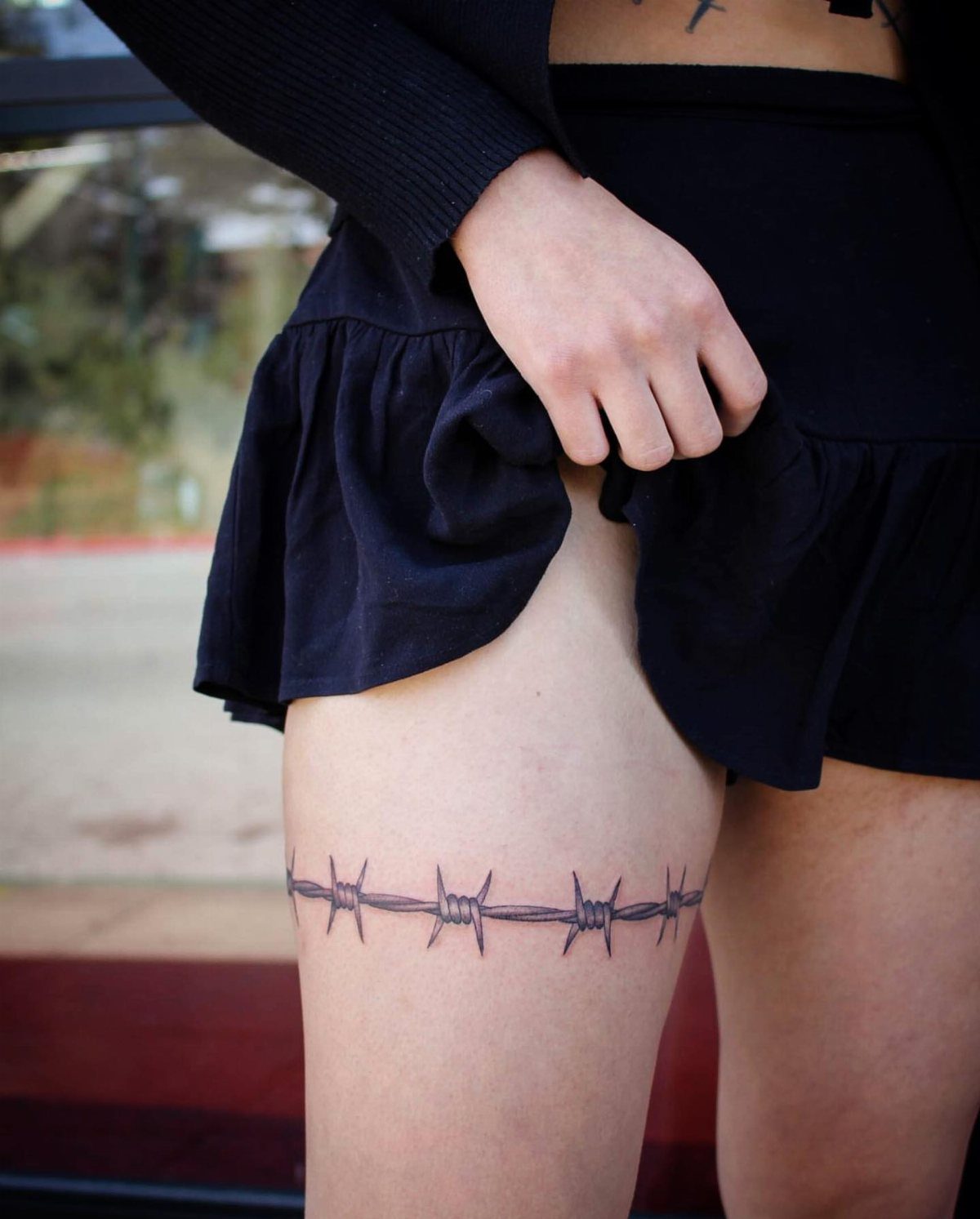 Barbed wire tattoo wrapping around the upper thigh of a person wearing black.