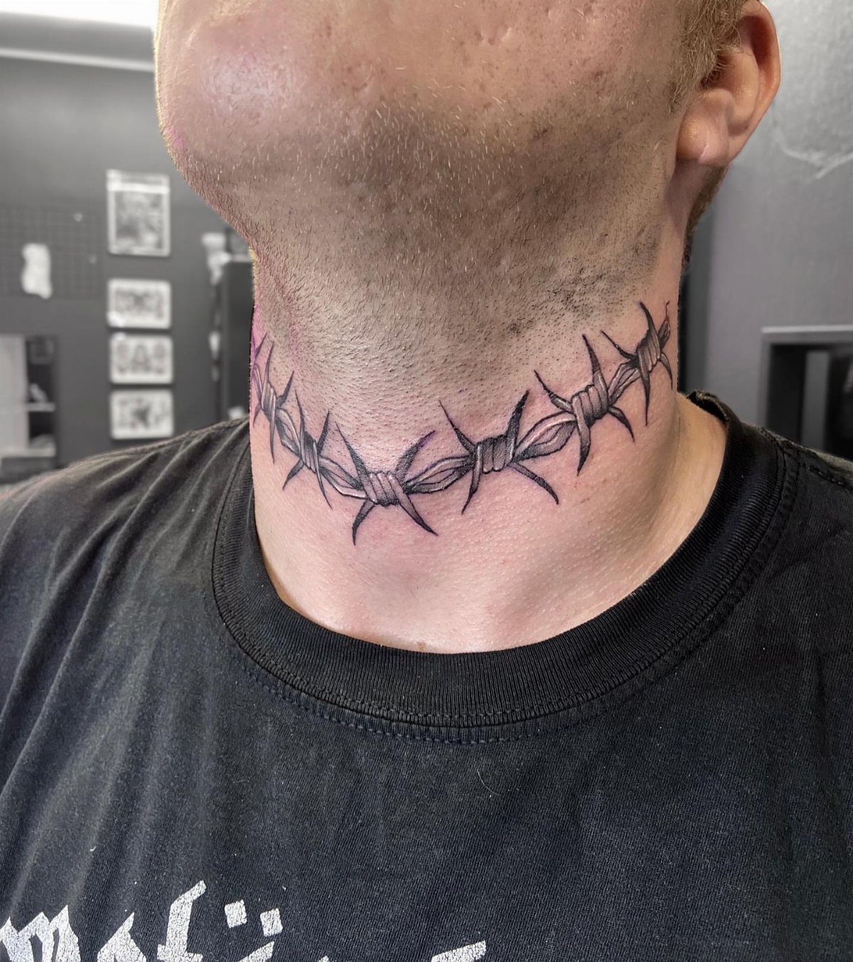 Barbed wire tattoo wrapped around the neck of a person wearing black.