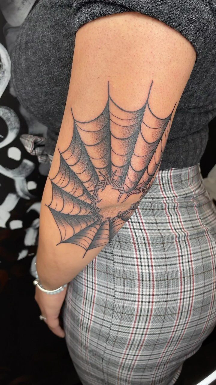 Spider web tattoo with barbed wire on a person's upper arm