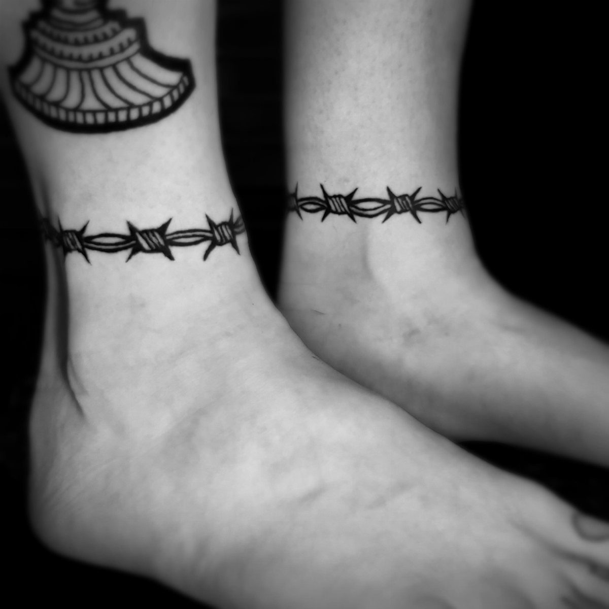 Barbed wire tattoos wrapped around the ankles of two people.