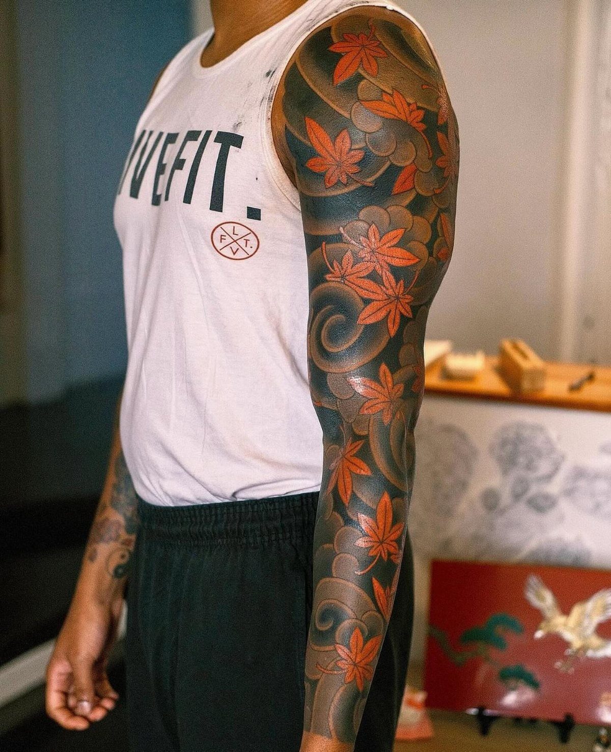 Full arm sleeve tattoo with orange maple leaves on brown skin.