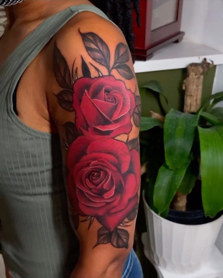 Two red rose tattoos with black leaves on a brown skin arm