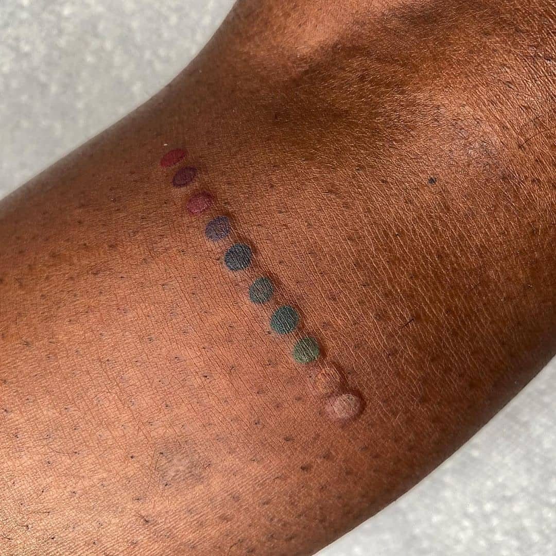 Brown skin with a diagonal row of small, colorful tattooed ink dots.