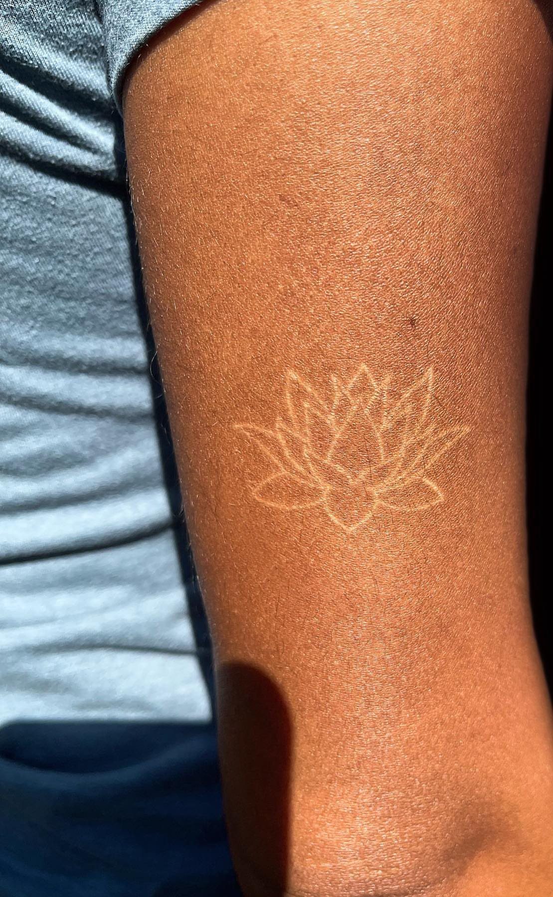 White ink lotus flower tattoo on a person's brown-skinned arm.