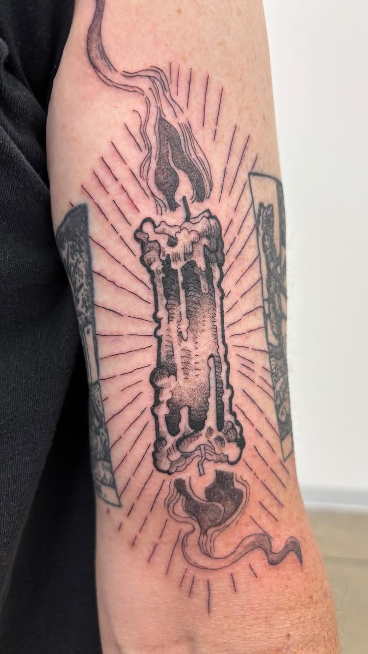 Burning candle tattoo on a forearm with melting wax and radiating light lines.