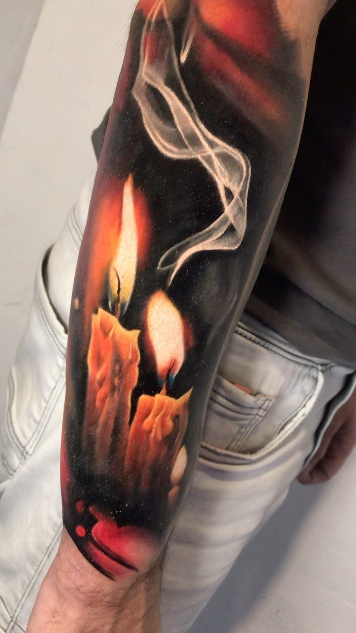 Two lit dripping candles with a swirling white smoke plume tattooed on a forearm.
