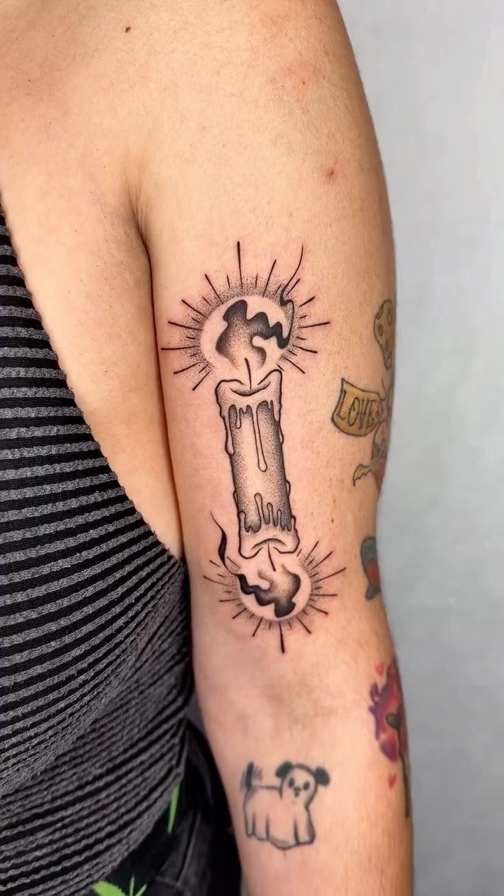 Double-ended candle tattoo with burning flames and dripping wax on an upper arm.