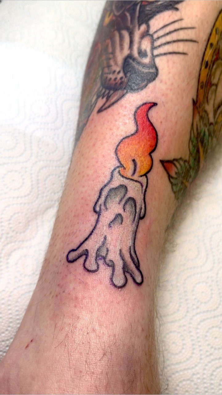 Melting candle tattoo with a bright orange flame on a person's arm.