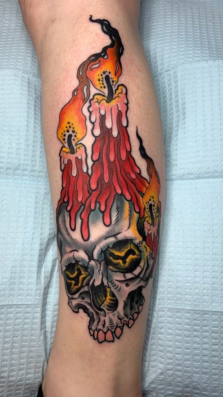 Skull tattoo with three red melting candles and orange flames on a leg