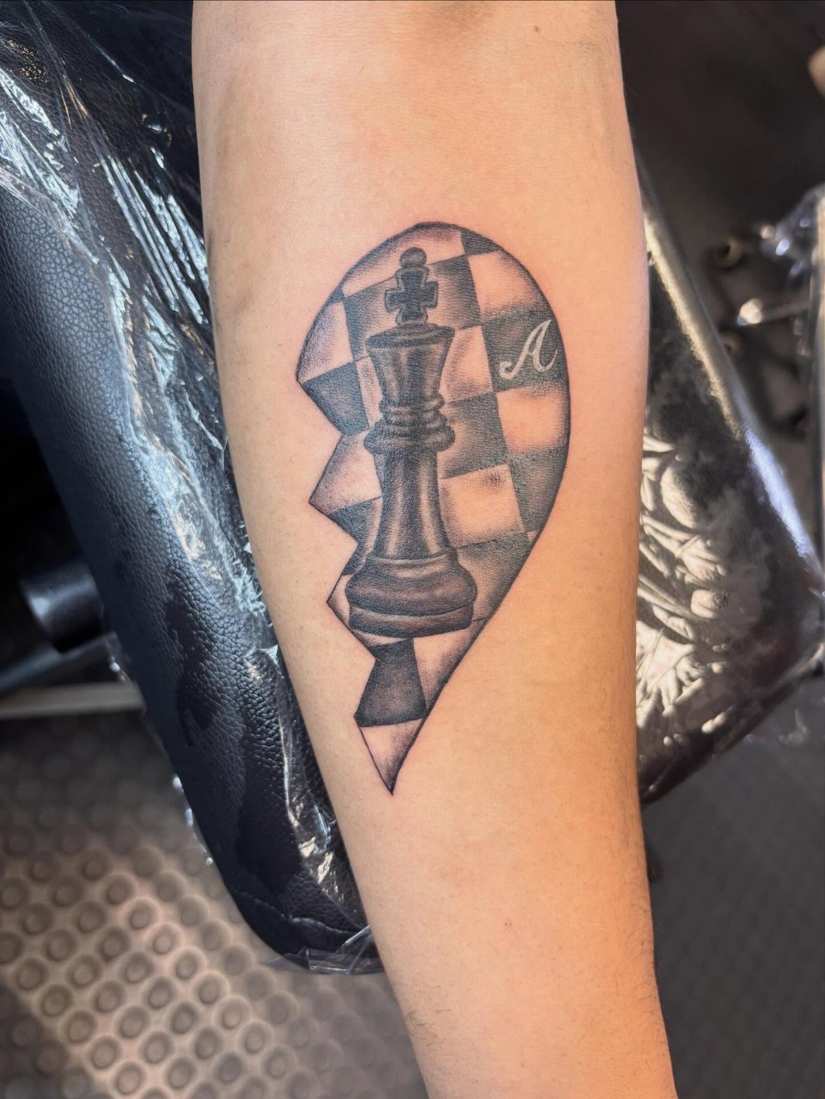 Chess king tattoo with a checkered background on a person's forearm.