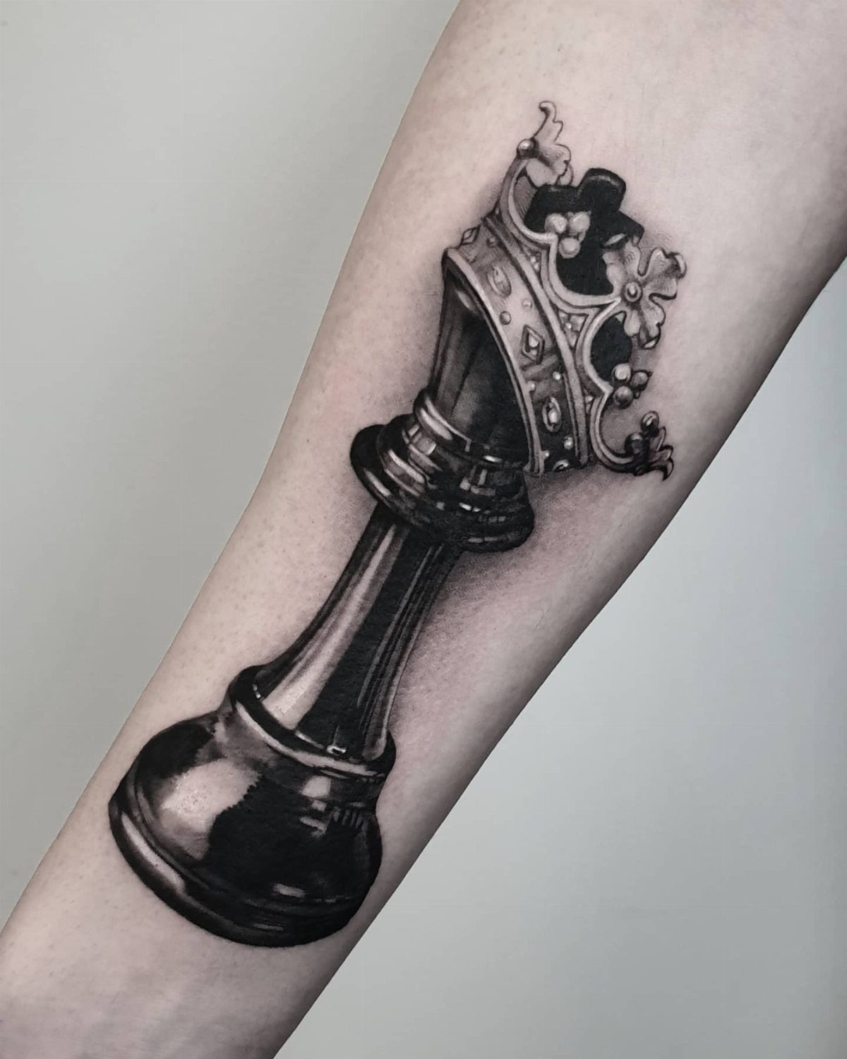 Chess king tattoo with realistic shading on a person's forearm.