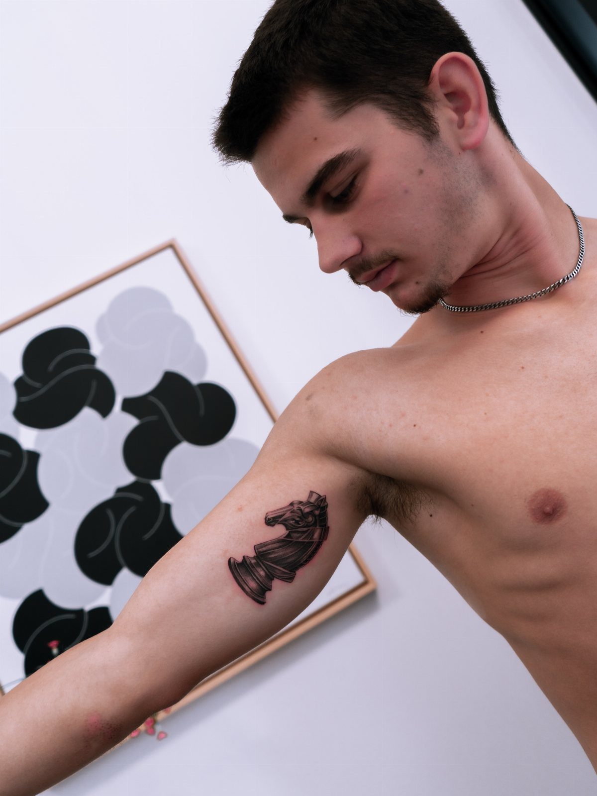 Chess knight tattoo on a man's upper arm with abstract art in background