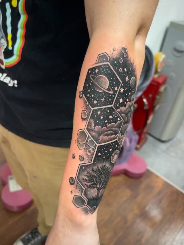 Geometric honeycomb tattoo on forearm featuring stars, clouds, a planet, and a tree.