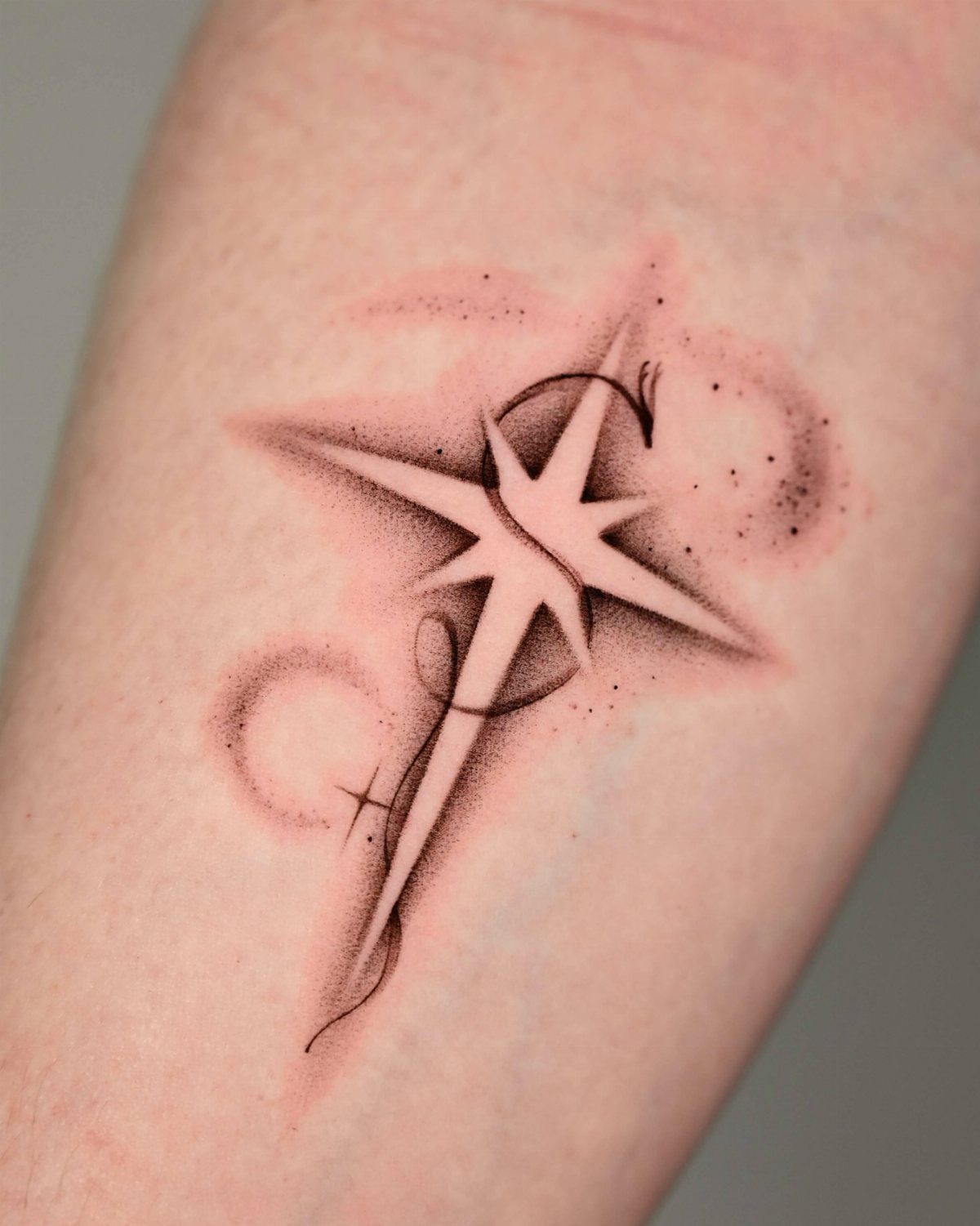 Four-pointed star tattoo with negative space center and soft grey shaded clouds.