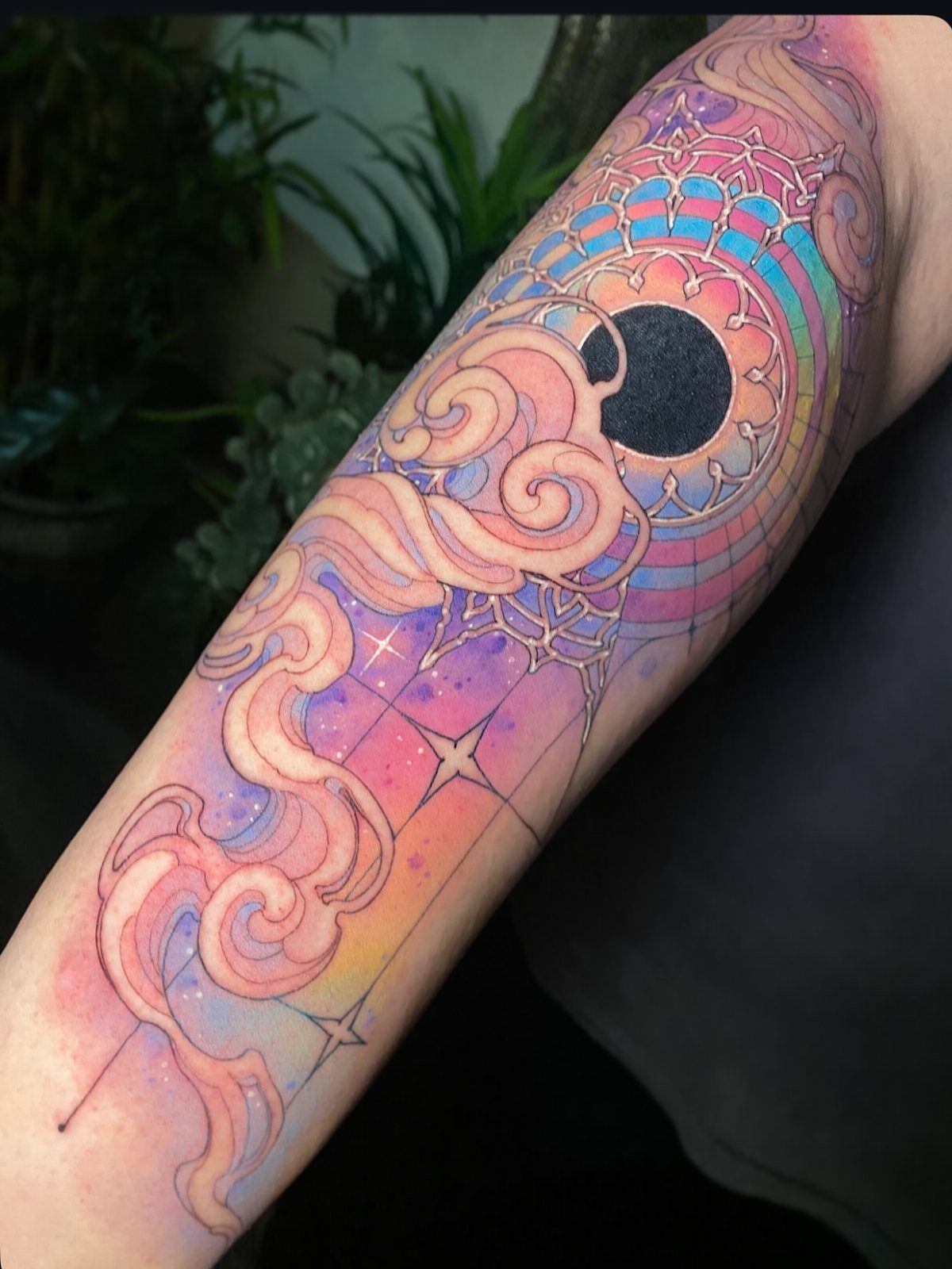 Colorful arm tattoo with swirling clouds, stars, a black moon, and a mandala.