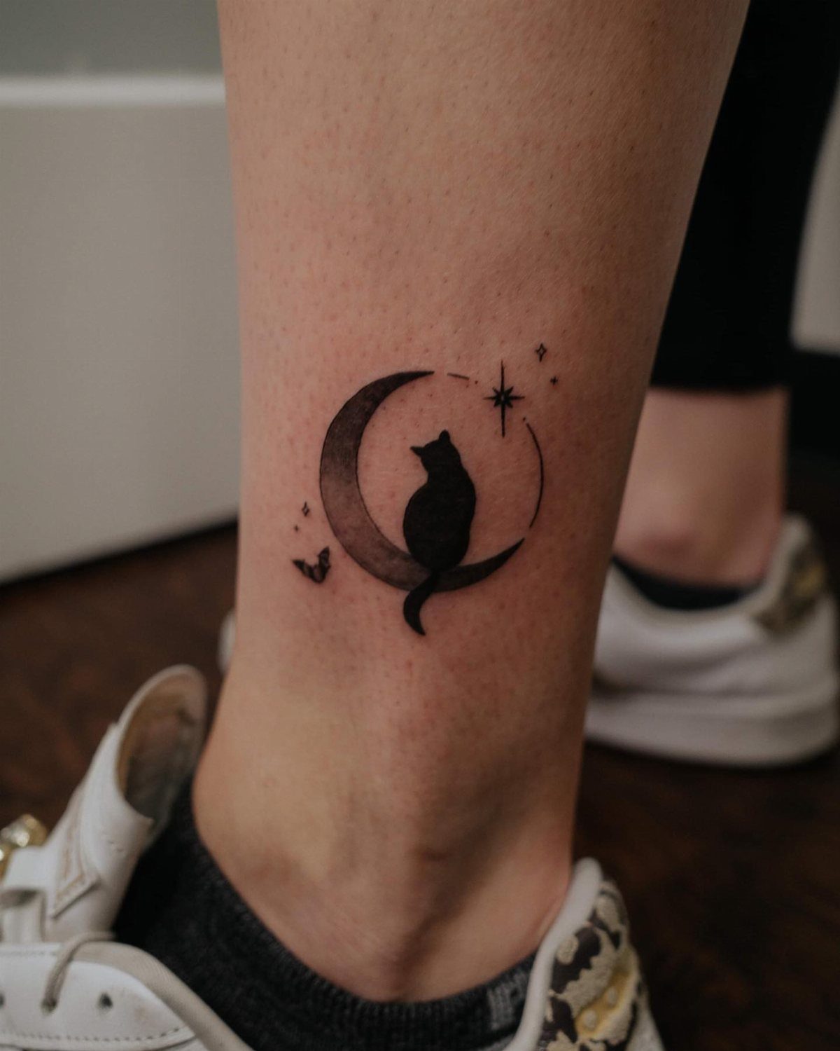 Cat silhouette tattoo inside a crescent moon on a person's ankle