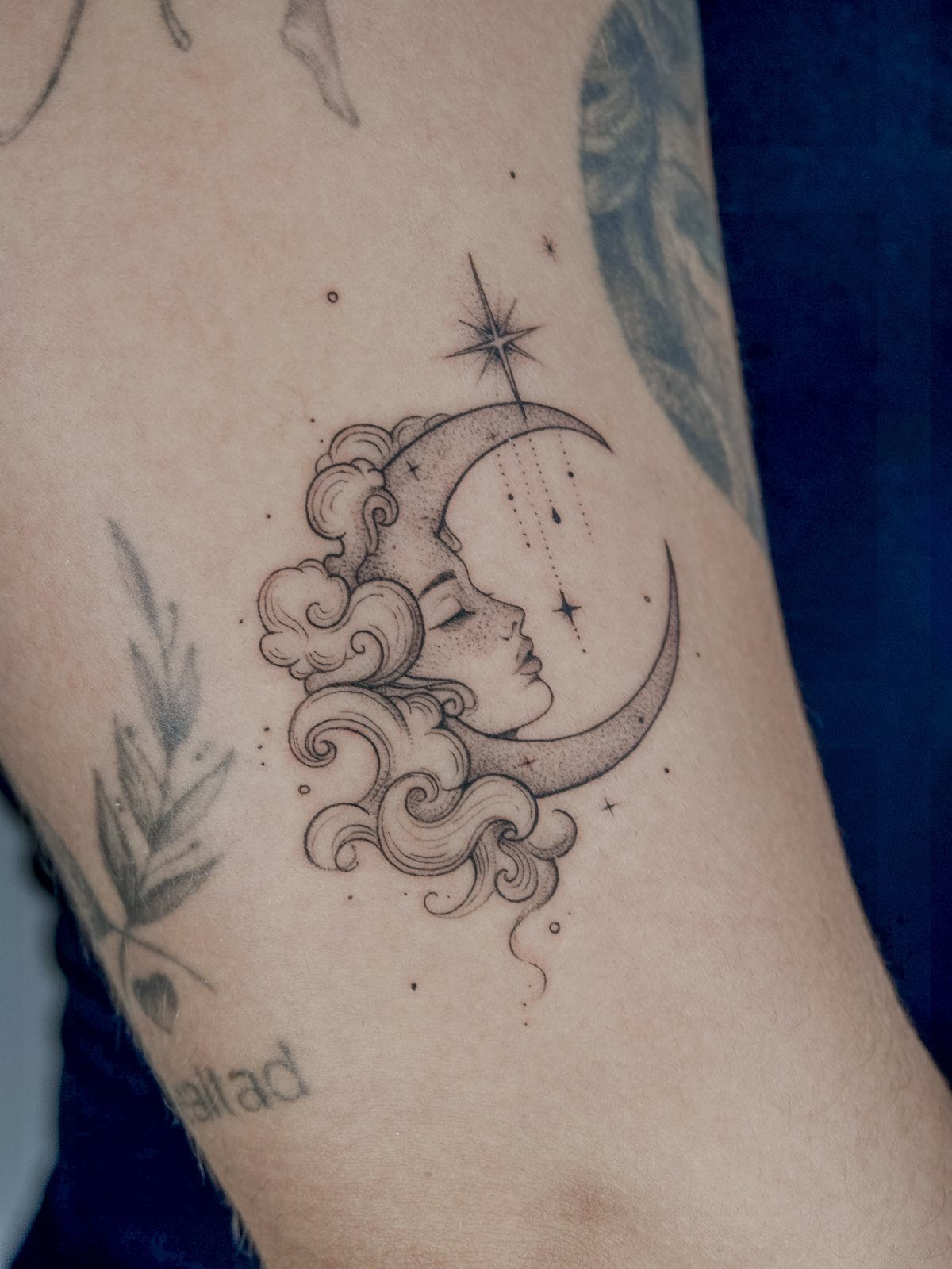 Crescent moon tattoo with a woman's profile face and swirling clouds on skin