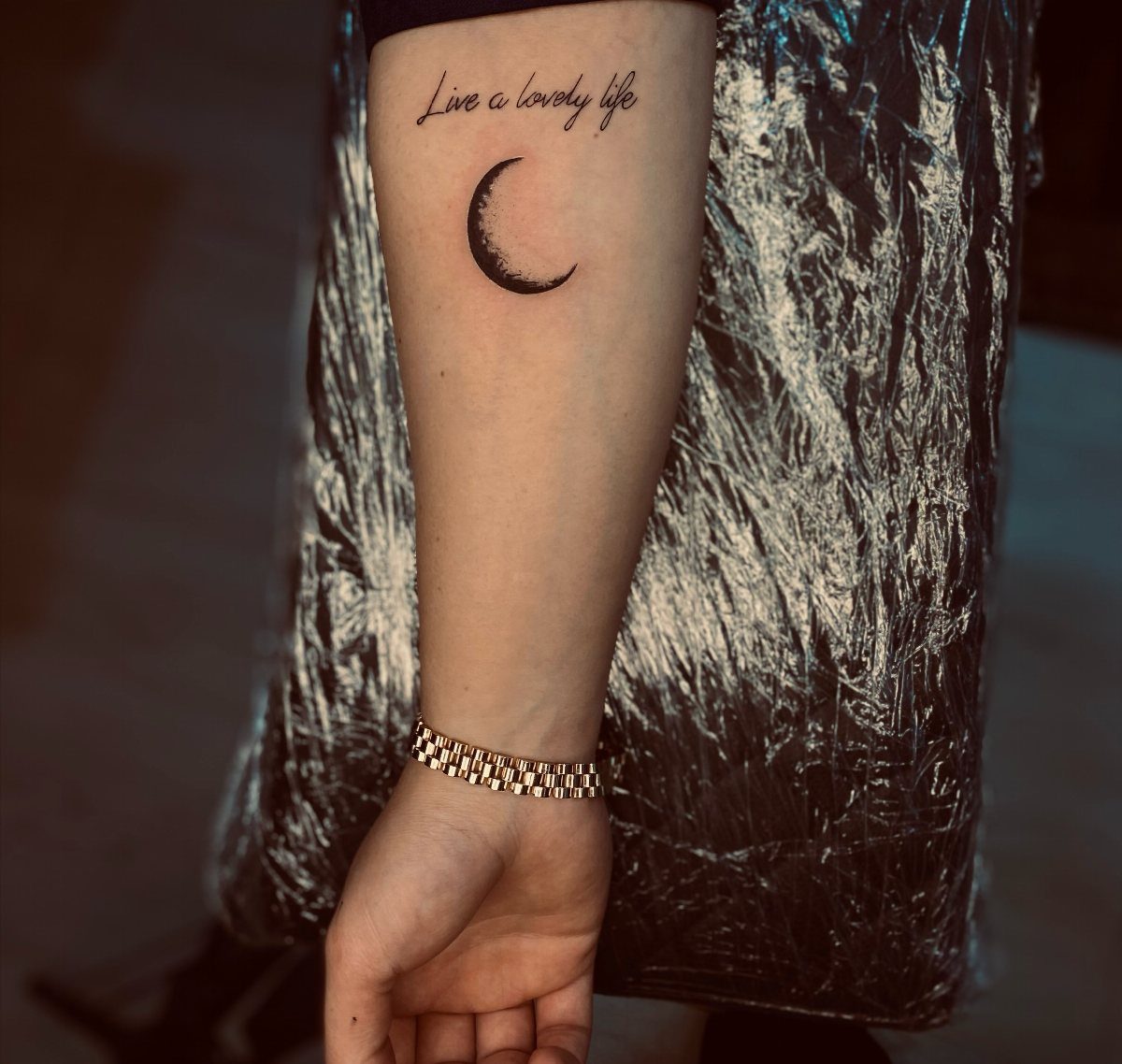 Crescent moon tattoo with the quote Live a lovely life on a forearm
