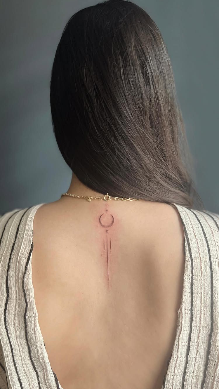 Minimalist crescent moon tattoo with a vertical line on a person's upper back.