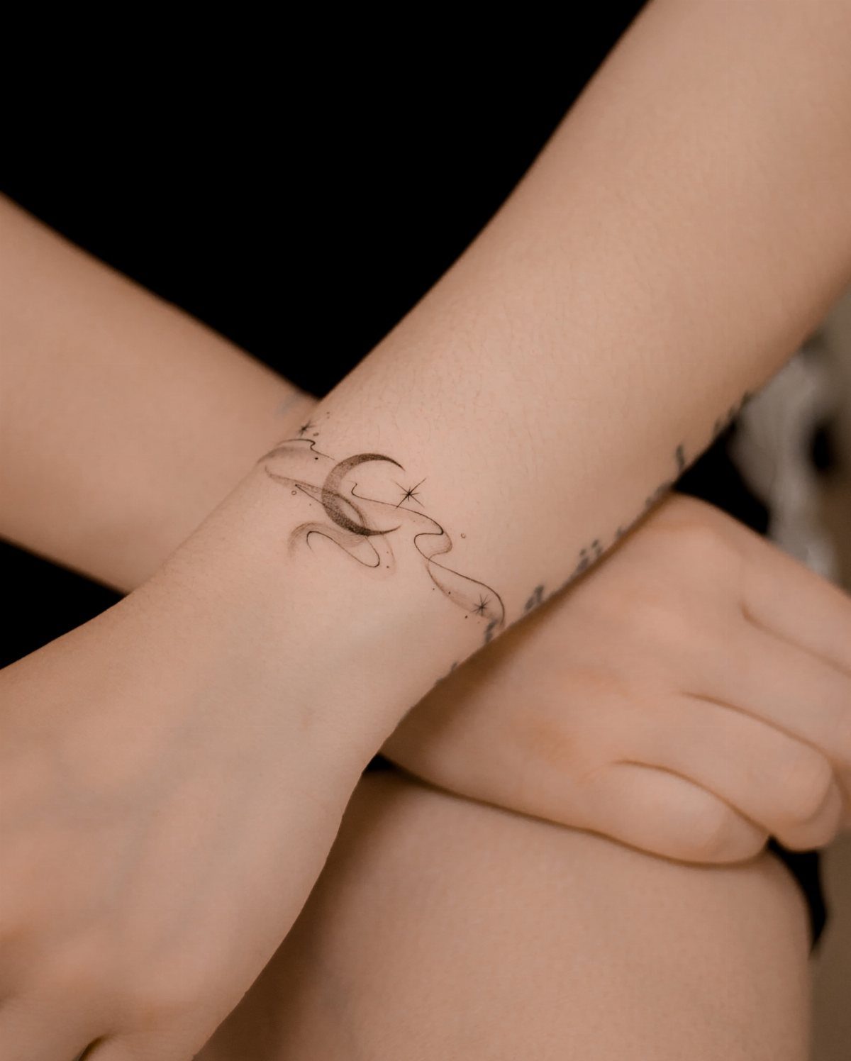 Small black ink crescent moon tattoo with a star on an inner wrist
