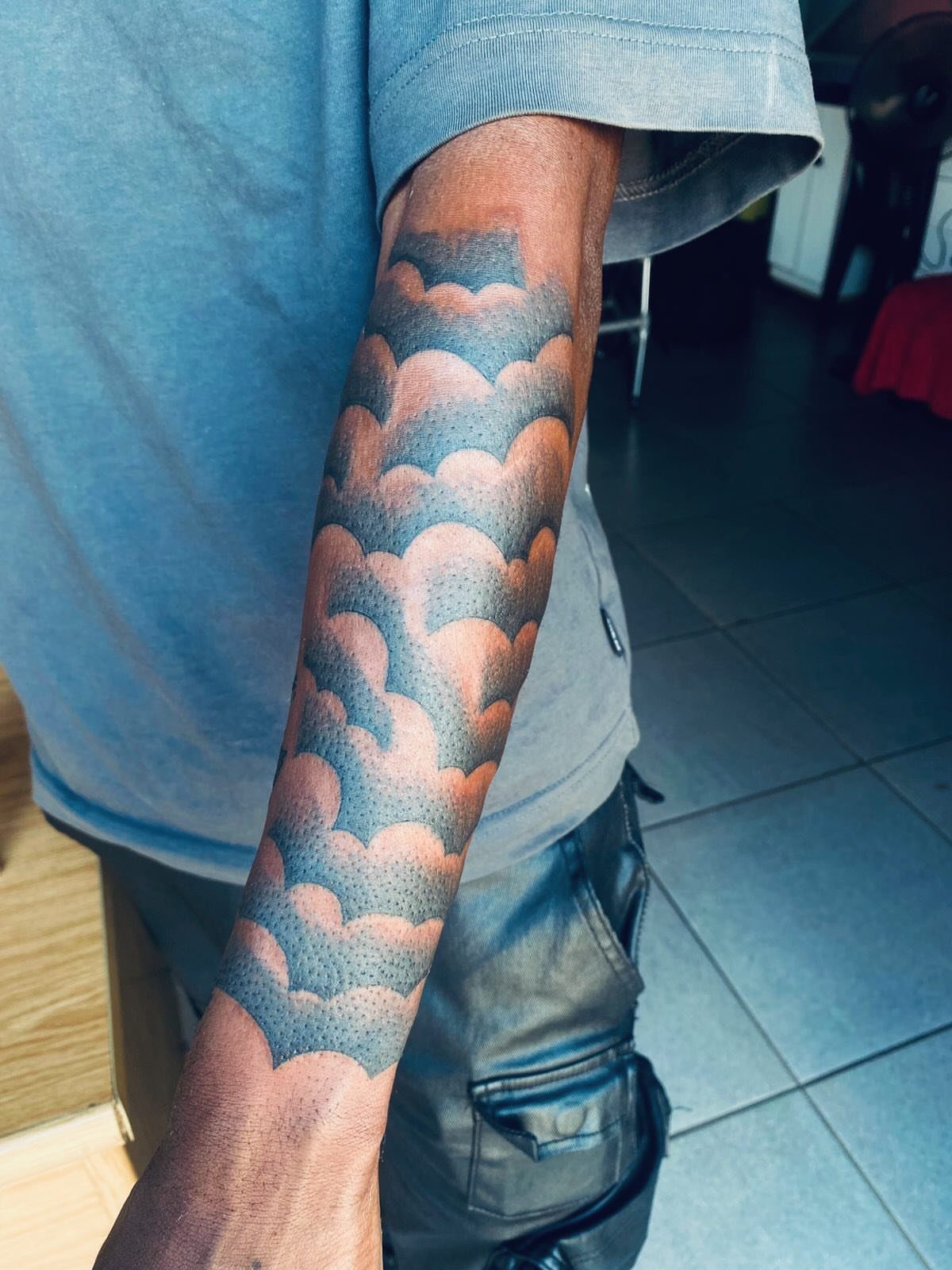 Forearm tattoo of stylized dark grey and black clouds with stippled shading.