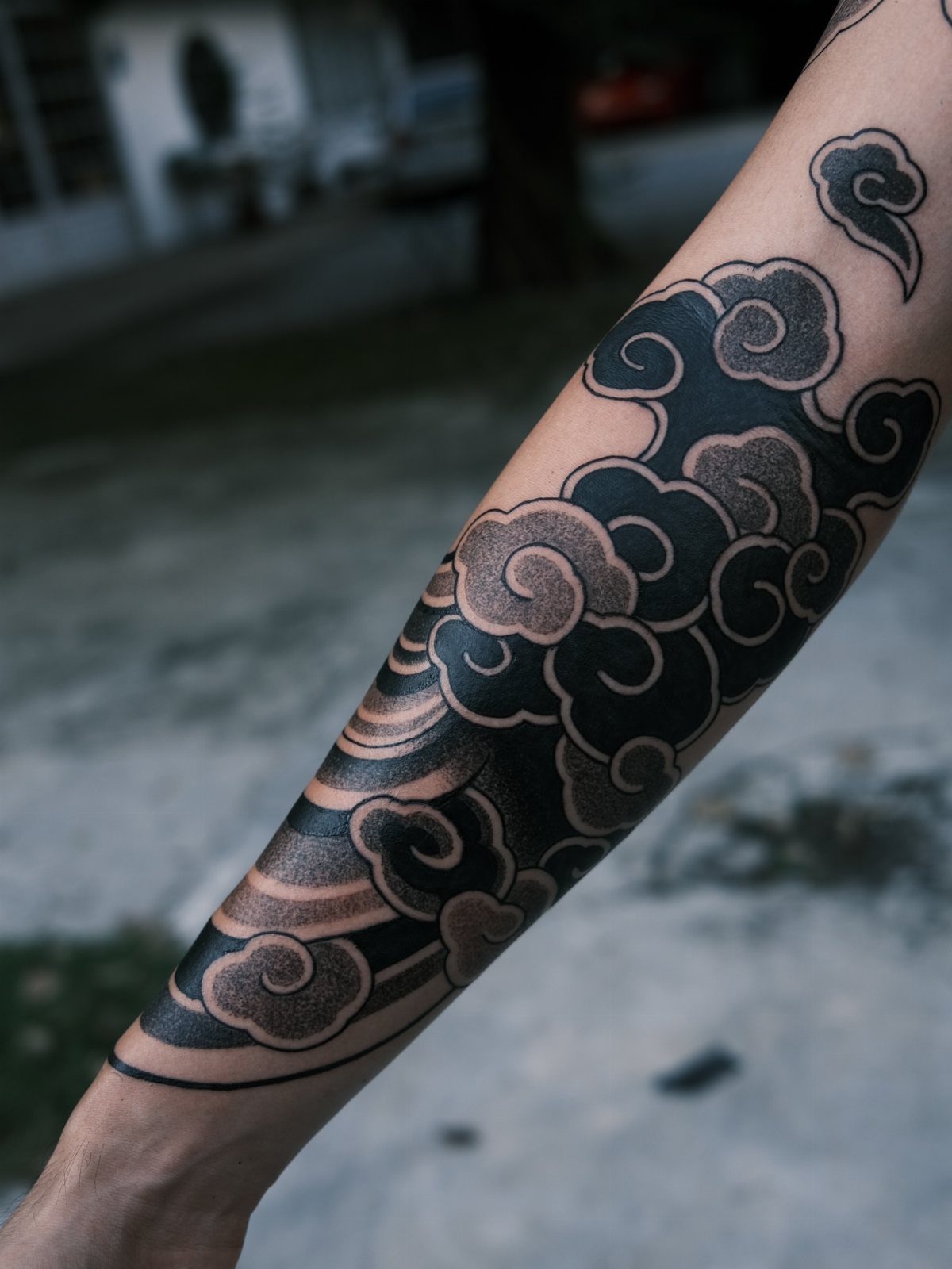 Stylized black Japanese cloud tattoo covering a person's forearm with grey shading.
