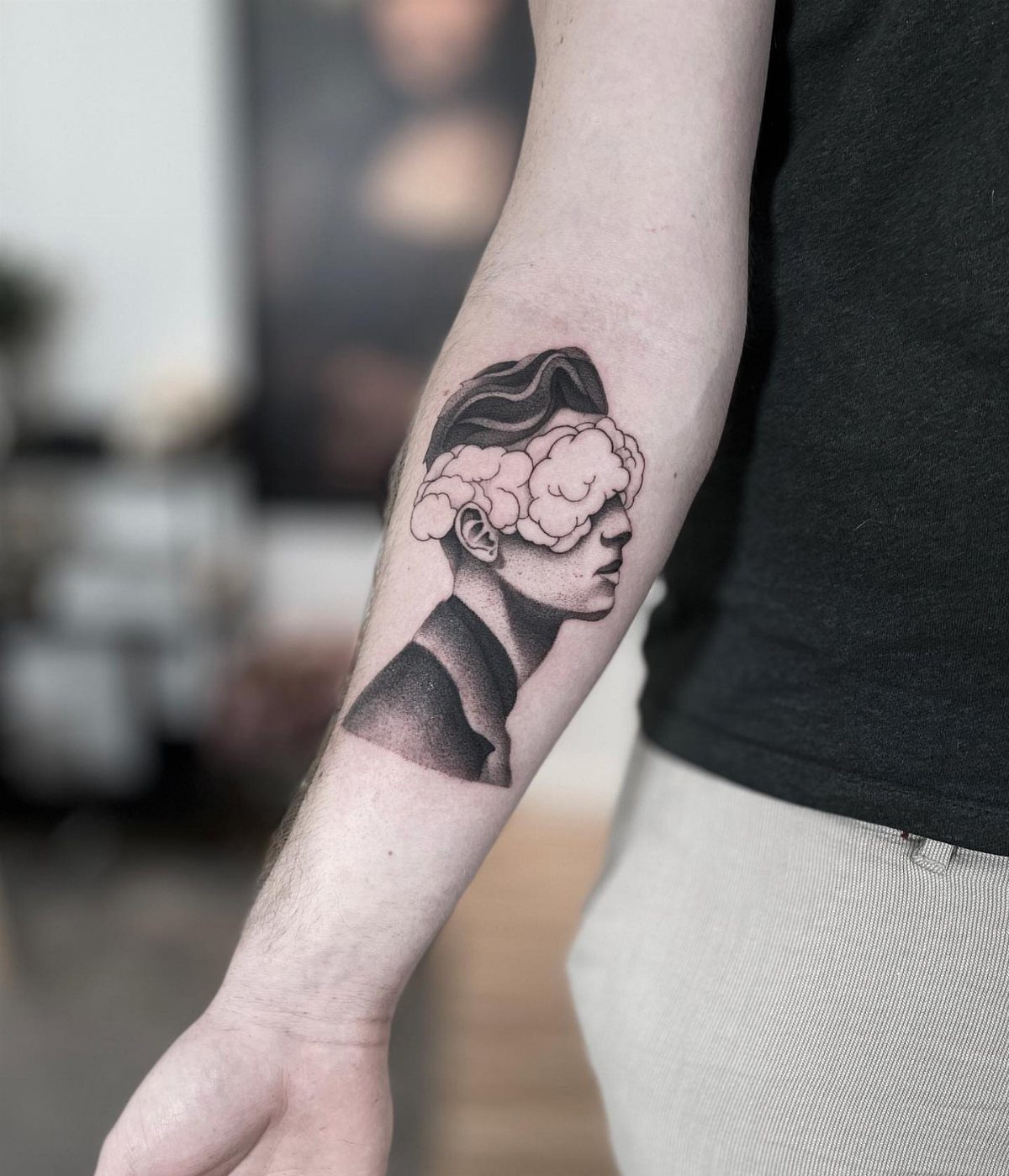 Forearm tattoo of a man's profile with clouds obscuring his eyes.