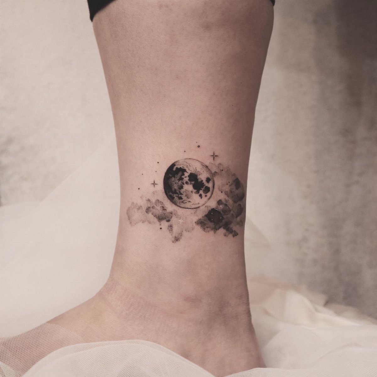 Moon and dark cloud tattoo on a person's ankle with small star accents