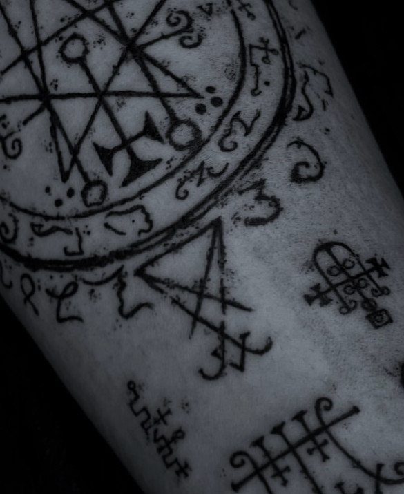 Occult alchemical symbols and a complex circular sigil tattooed in black ink on skin