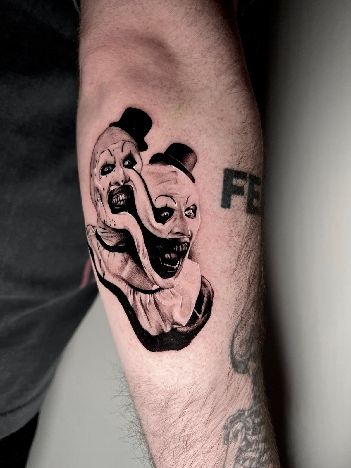 Creepy clown tattoo with top hats and sharp teeth on a person's forearm.