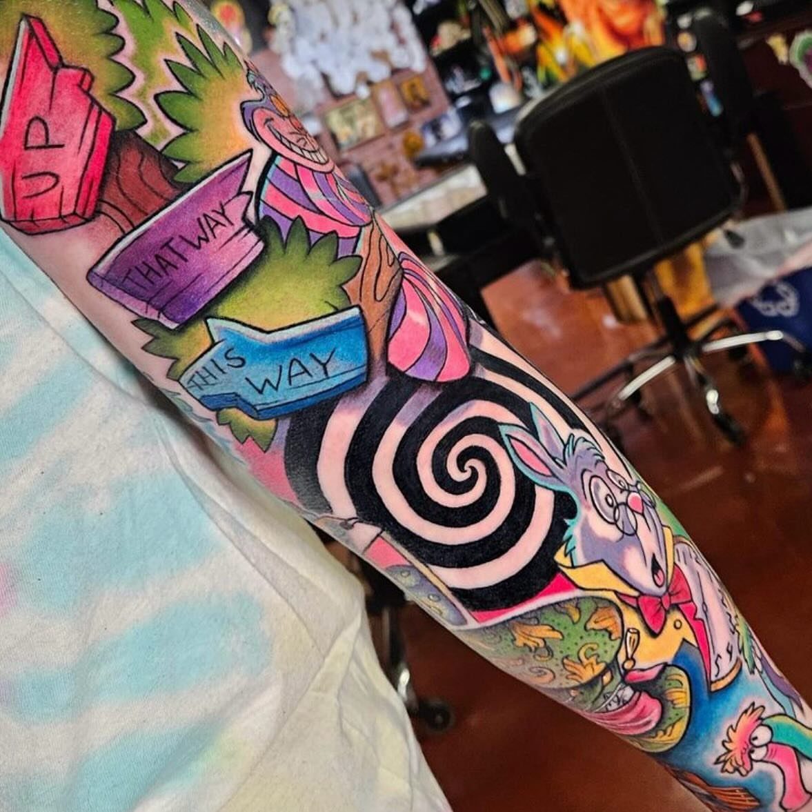 Colorful sleeve tattoo featuring Alice in Wonderland characters and a swirling black and white spiral.