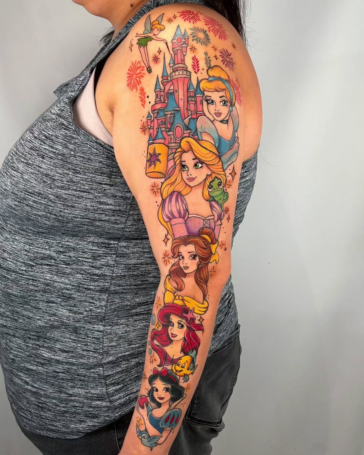 Full-sleeve tattoo of colorful Disney princess portraits and a castle on an arm.