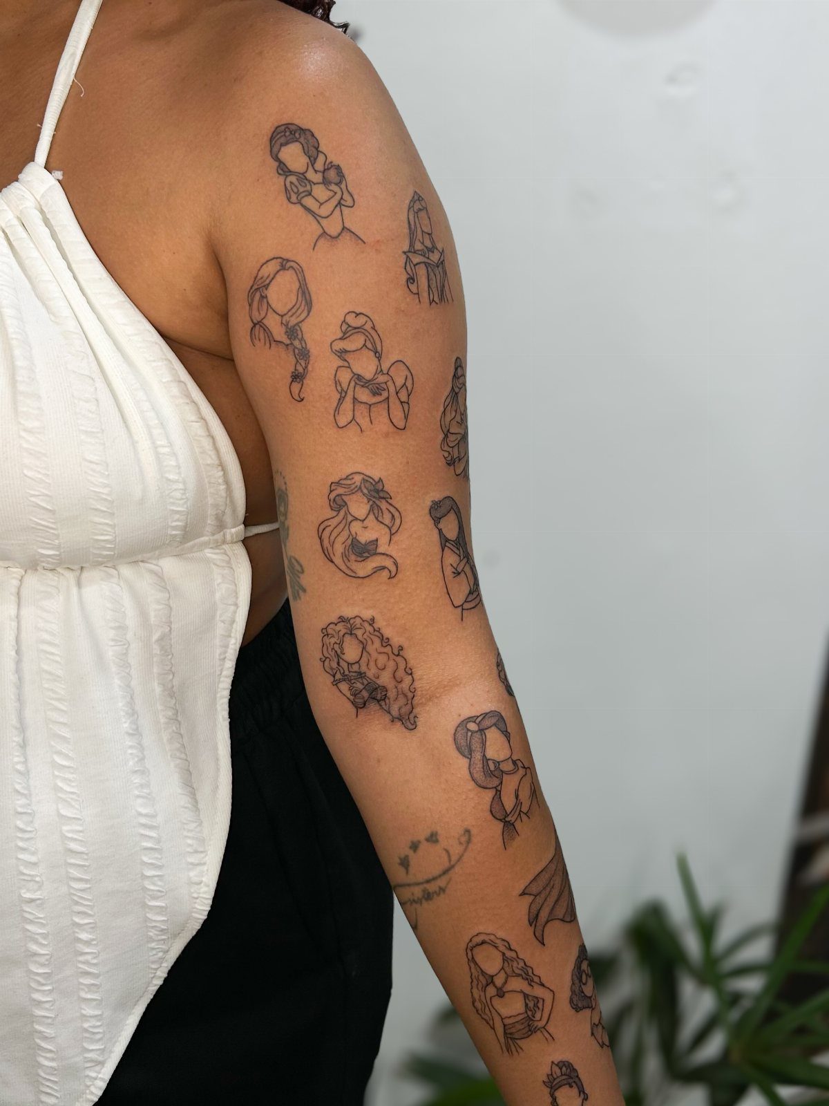Arm with a vertical stack of small black line art Disney character tattoos.