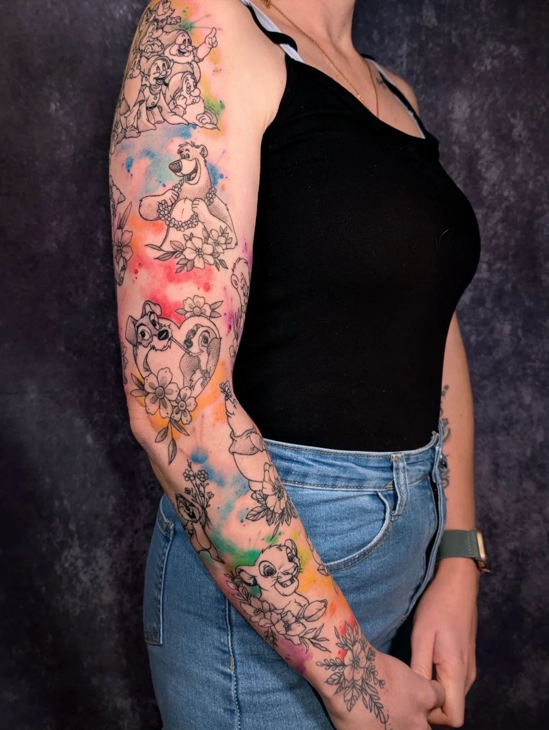 Disney character sleeve tattoo with vibrant watercolor splashes on a person's arm.