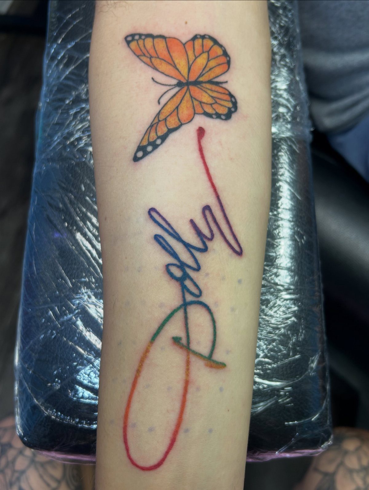 Butterfly tattoo and colorful Dolly script on a person's forearm.